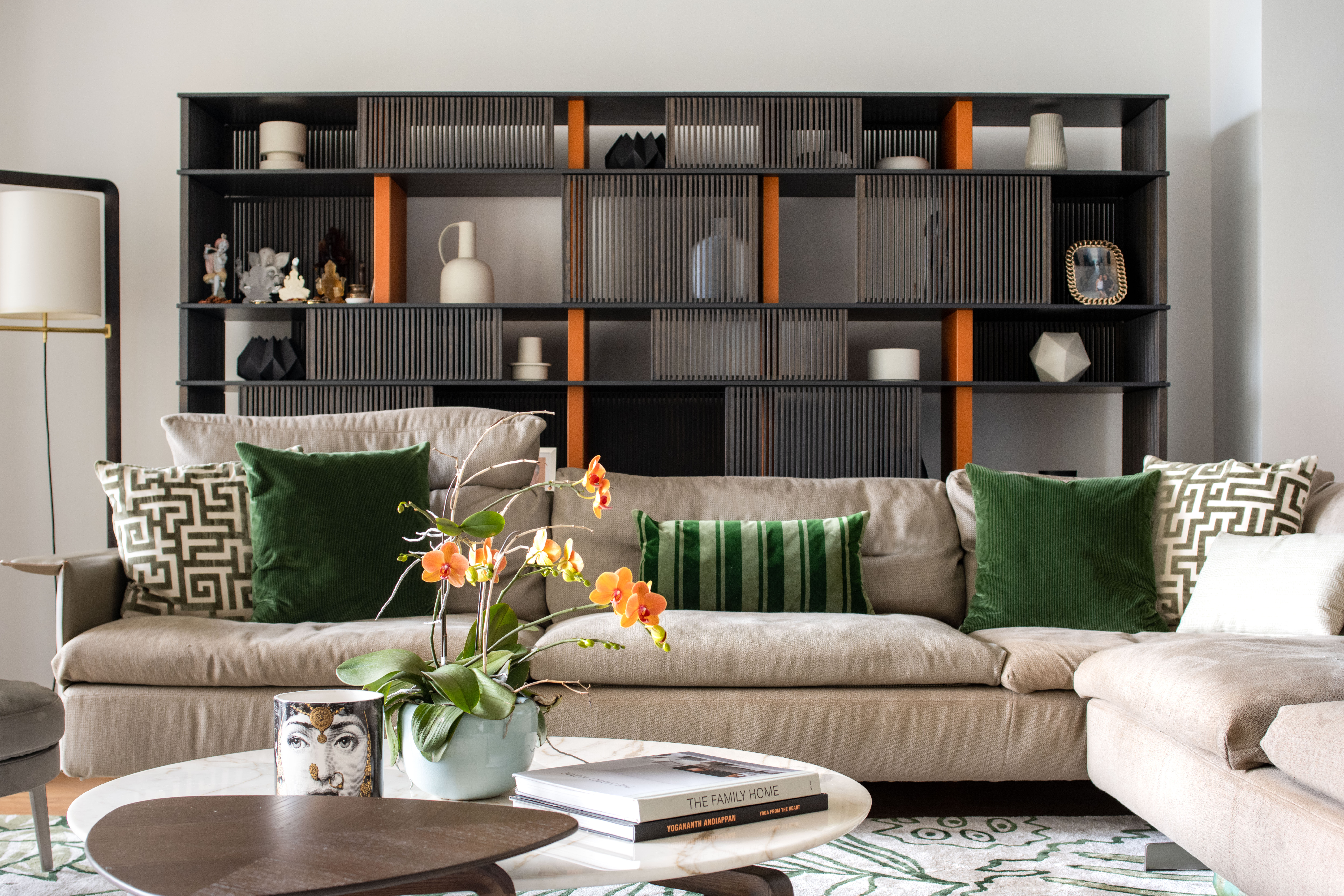 A Zip Code 888 living room with green velvet cushions, a sculptural dark shelving wall and bright orchids.